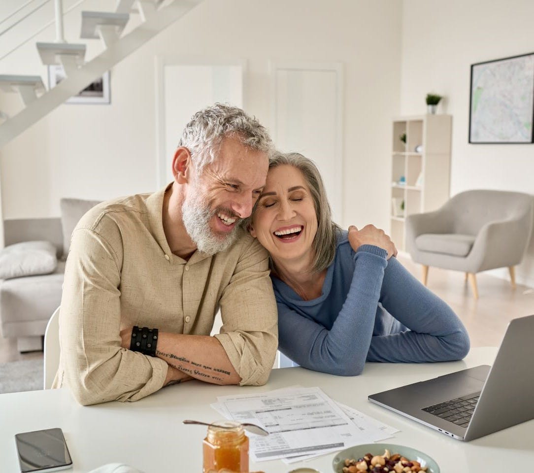 Happy mature older couple sitting at home with a laptop, laughing.