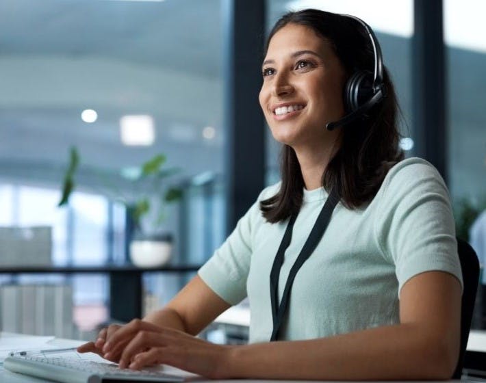 Smiling dark haired female typing on computer wearing a headset.