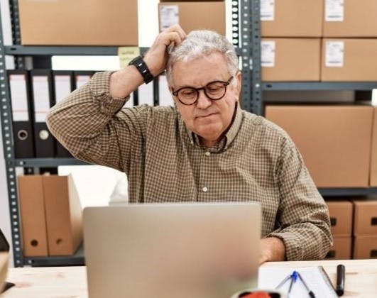 Older man working at small business with laptop confused and wondering about a question.