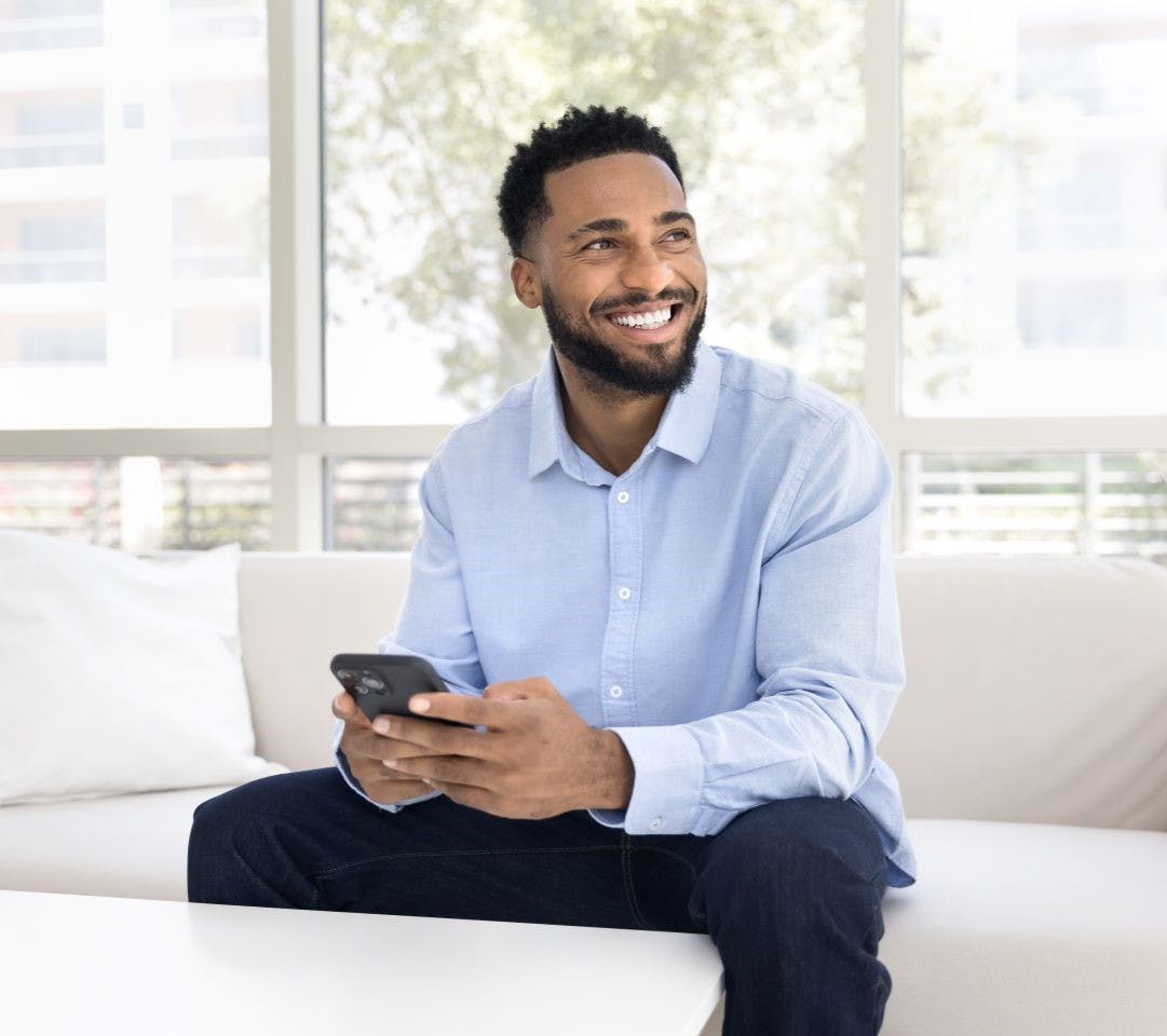 Professional man wearing a smart blue shirt sitting on a sofa holding a phone.