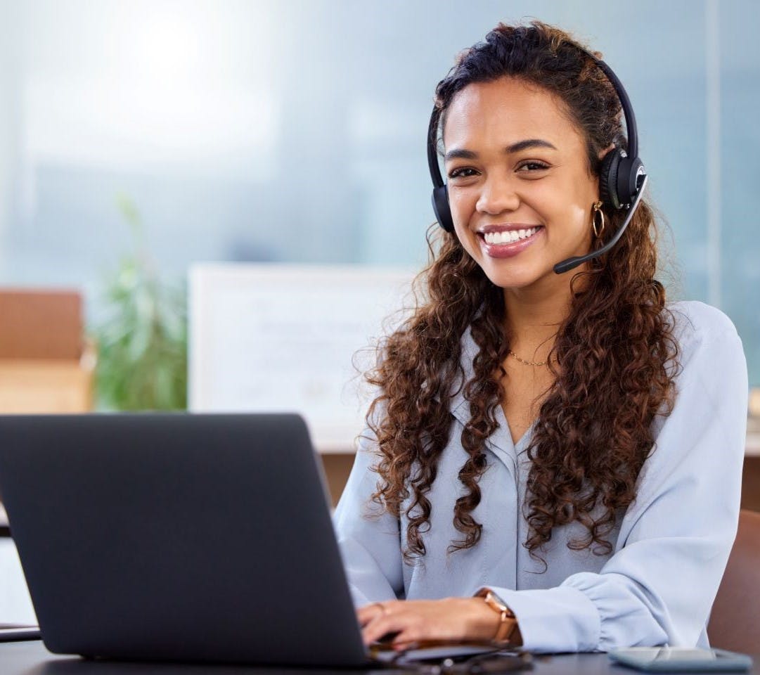 Smiling, curly haired, Asian female receptionist wearing a headset.