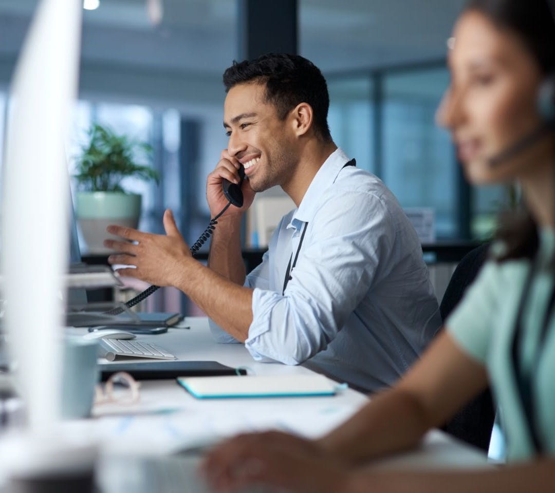 Smiling male receptionist on the phone whilst working in a call centre.