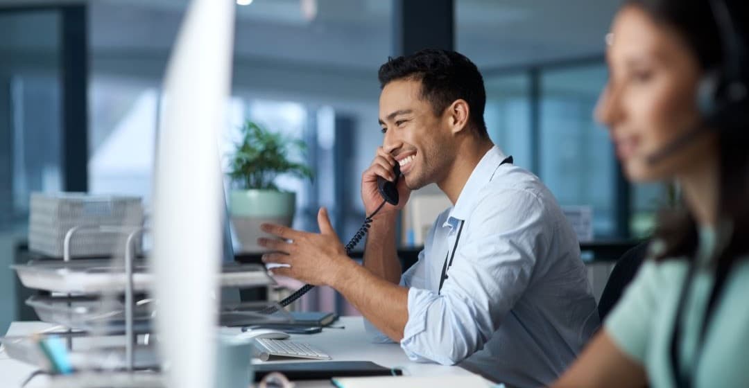 Smiling male receptionist on the phone whilst working in a call centre.