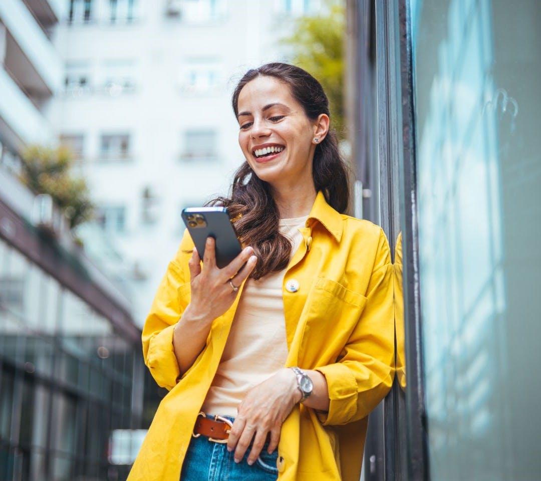 Brunette female wearing a yellow blazer smiling at her phone.