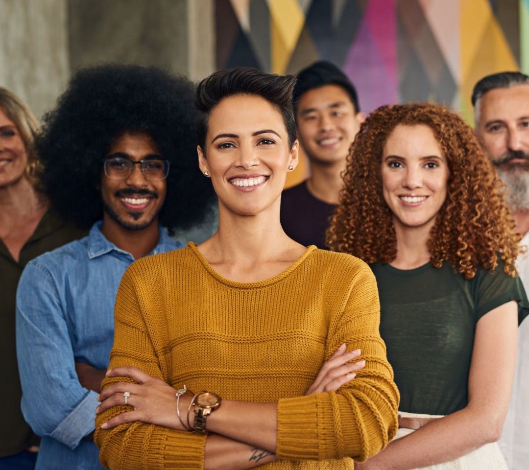 Happy, diverse team of employees with good employee wellbeing smiling with arms crossed.