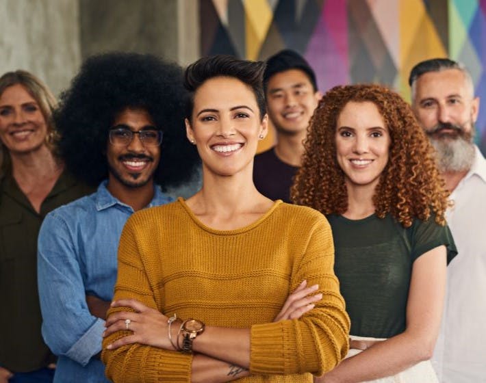 Happy, diverse team of employees with good employee wellbeing smiling with arms crossed.