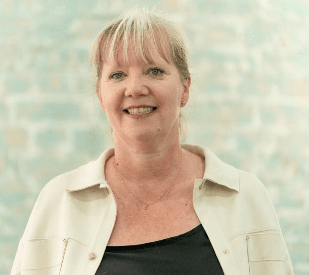 Portrait of smiling blonde female telephone answering Chief Operating Manager Ceri Henfrey on a blue brick background.