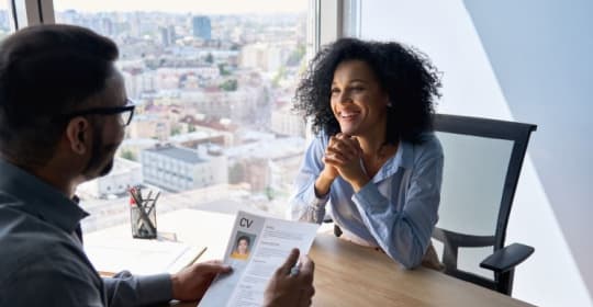 Friendly interview between Indian businessman hr director holding paper cv hiring for job female African American applicant manager sitting in contemporary office.