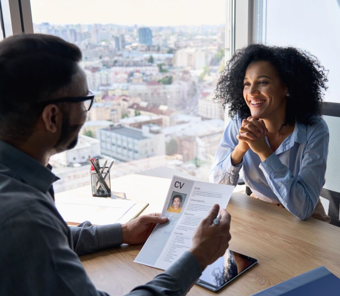 Friendly interview between Indian businessman hr director holding paper cv hiring for job female African American applicant manager sitting in contemporary office.