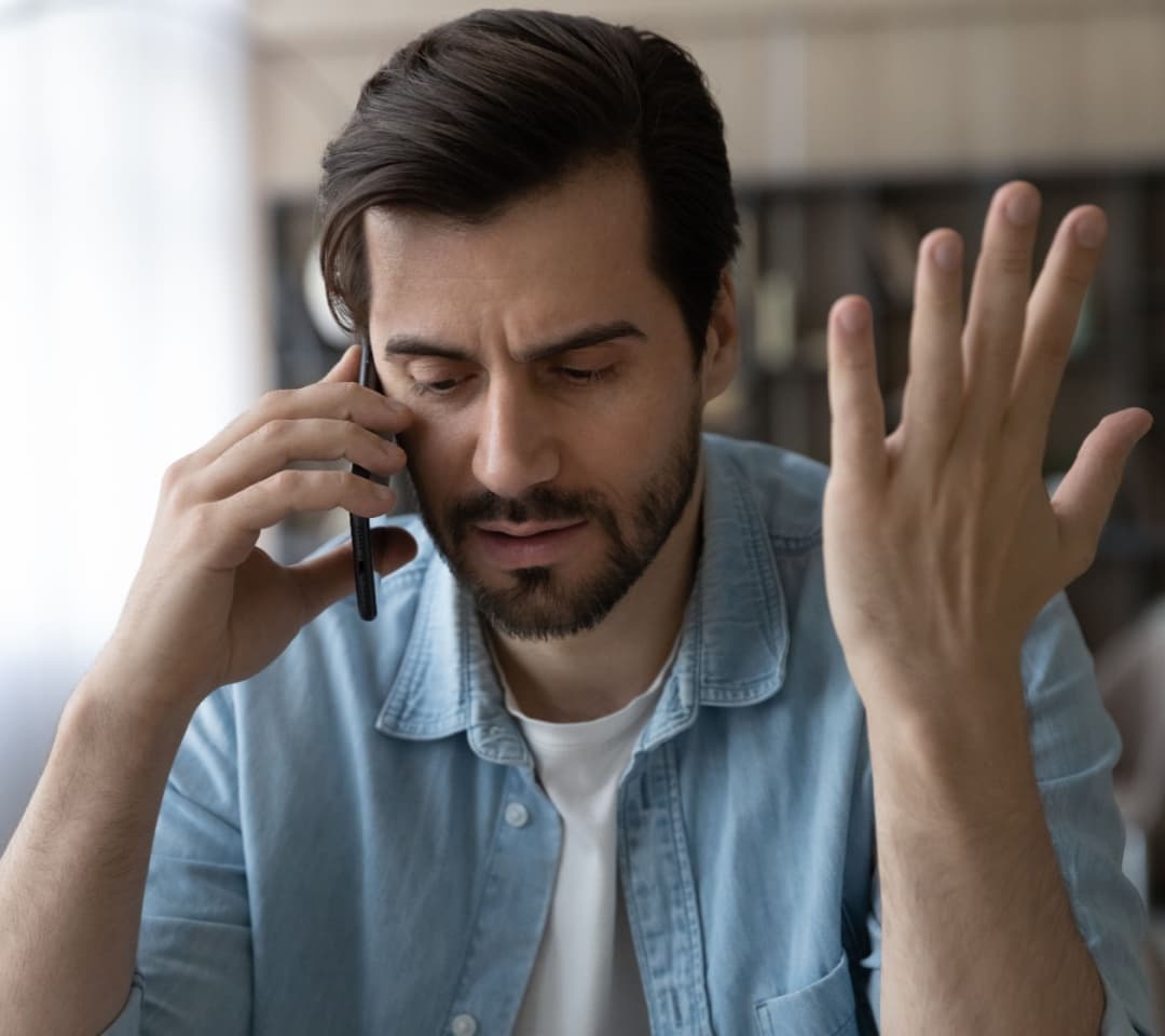 A man talking on the phone with his left hand in the air and a disappointed expression on his face after receiving bad customer service